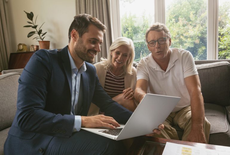 Front view of active senior Caucasian couple discussing with real estate agent over laptop in living room at home